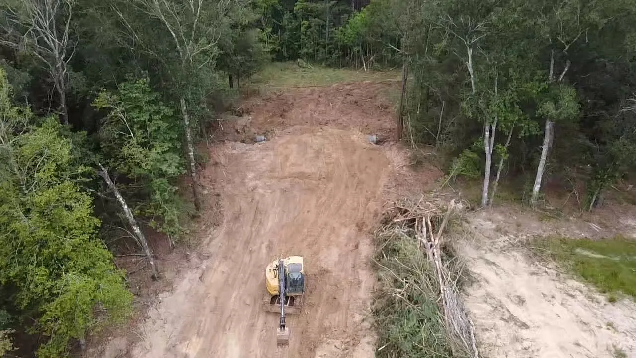 Excavator working a cleared corridor with culvert pipe staged